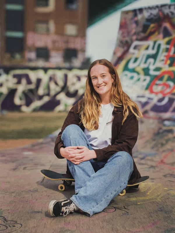 Linnéa sitter leendes på sin skejtboard i skejtboardrampen.