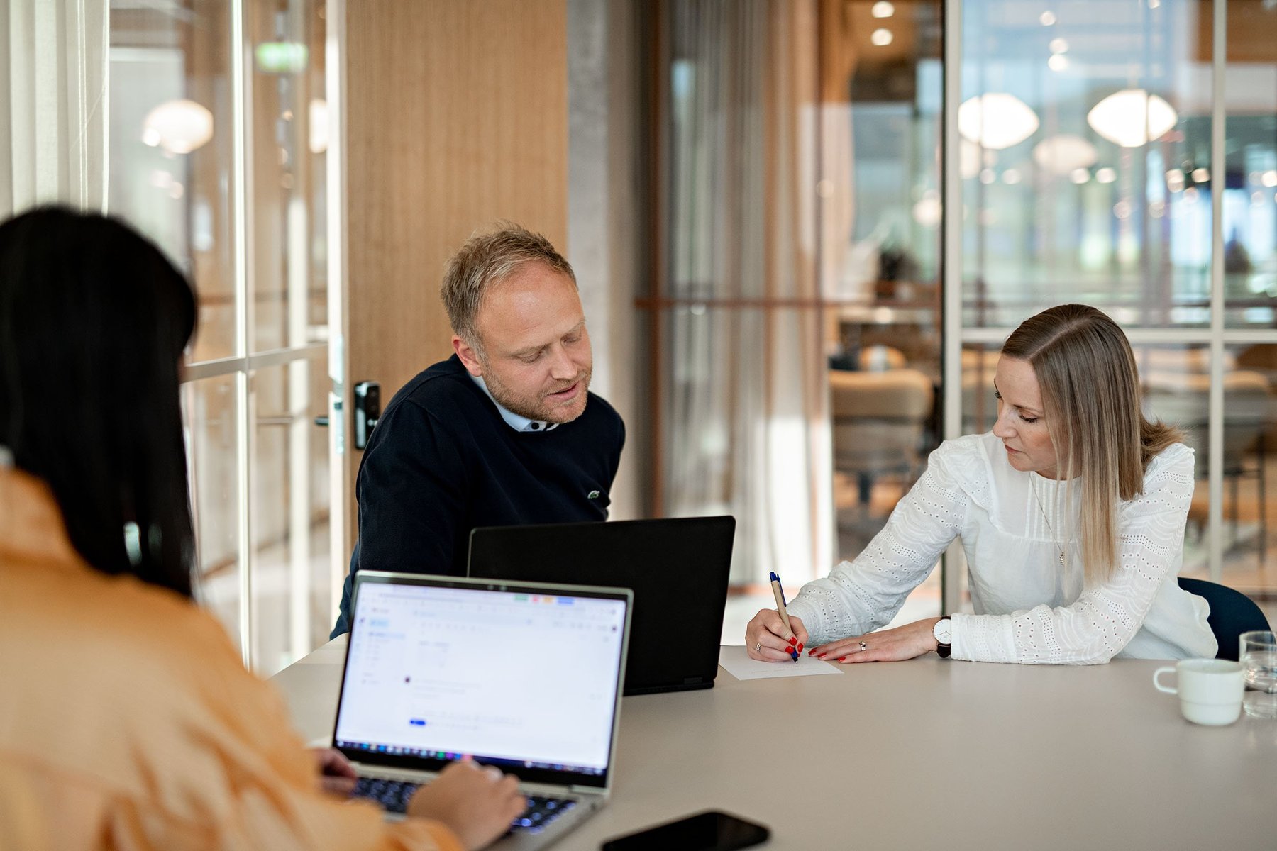 coworkers on laptop and writing on paper in meeting -Fullbredde