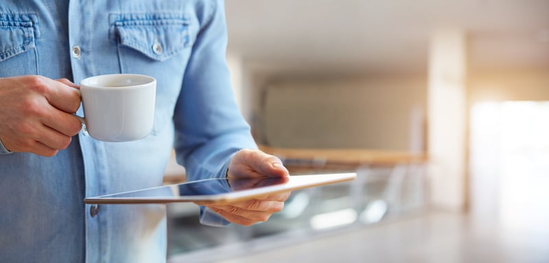 Person som håller i surfplatta och kaffekopp