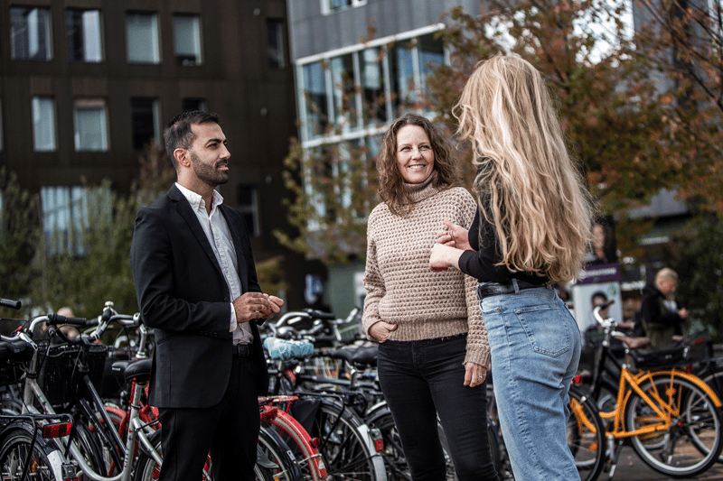 Tre personer pratar vid ett cykelställ