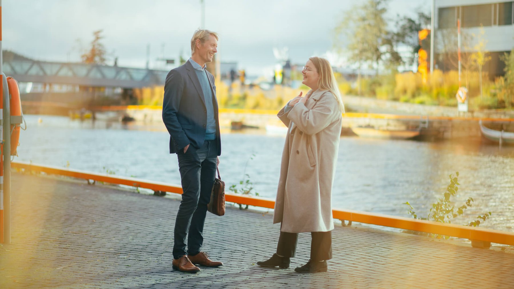 En dame og en mann med PC-veske står utendørs og ler sammen